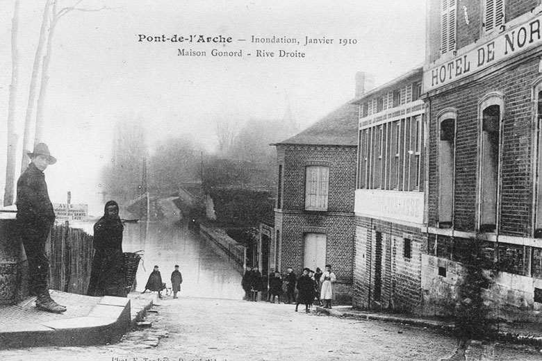 Carte postale 1910. Pont de l'Arche (27). habitants observant le niveau de l'eau (Eure et Seine) au droit de la Maison Gonord en rive droite