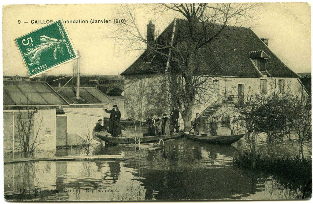 Carte postale 1910. Gaillon/Aubevoye (Le Val d'Hazey) (27). Source : collection Archives Départementales 27. Bâtiments inondés près du pont côté Aubevoye