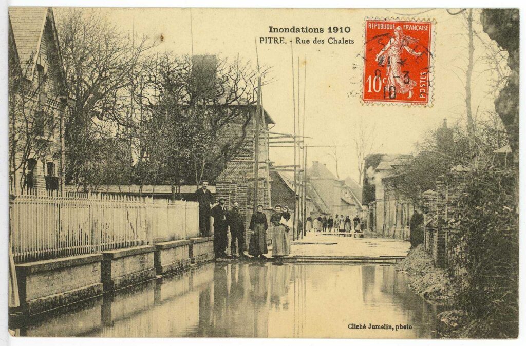 Carte postale 1910. Pîtres, rue des chalets. Route submergée au coeur du village et personnages dans la rue. Source : Collection Archives Départementales 27