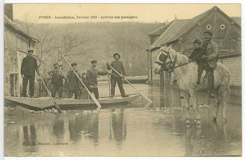 Carte postale 1910. Poses, inondation, février 1910, arrivée des passagers. Embarcation dans la rue et personnage dessus (source : Archives Départementales 27)